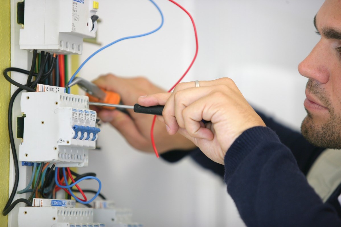 A man using a tool on an electrical board with wires.