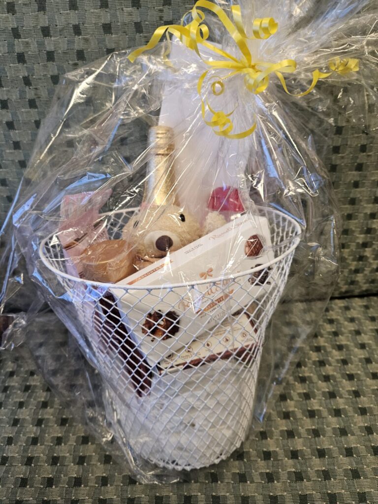 A gift basket wrapped in cellophane. It includes sparkling cider, candy, and a stuffed animal.