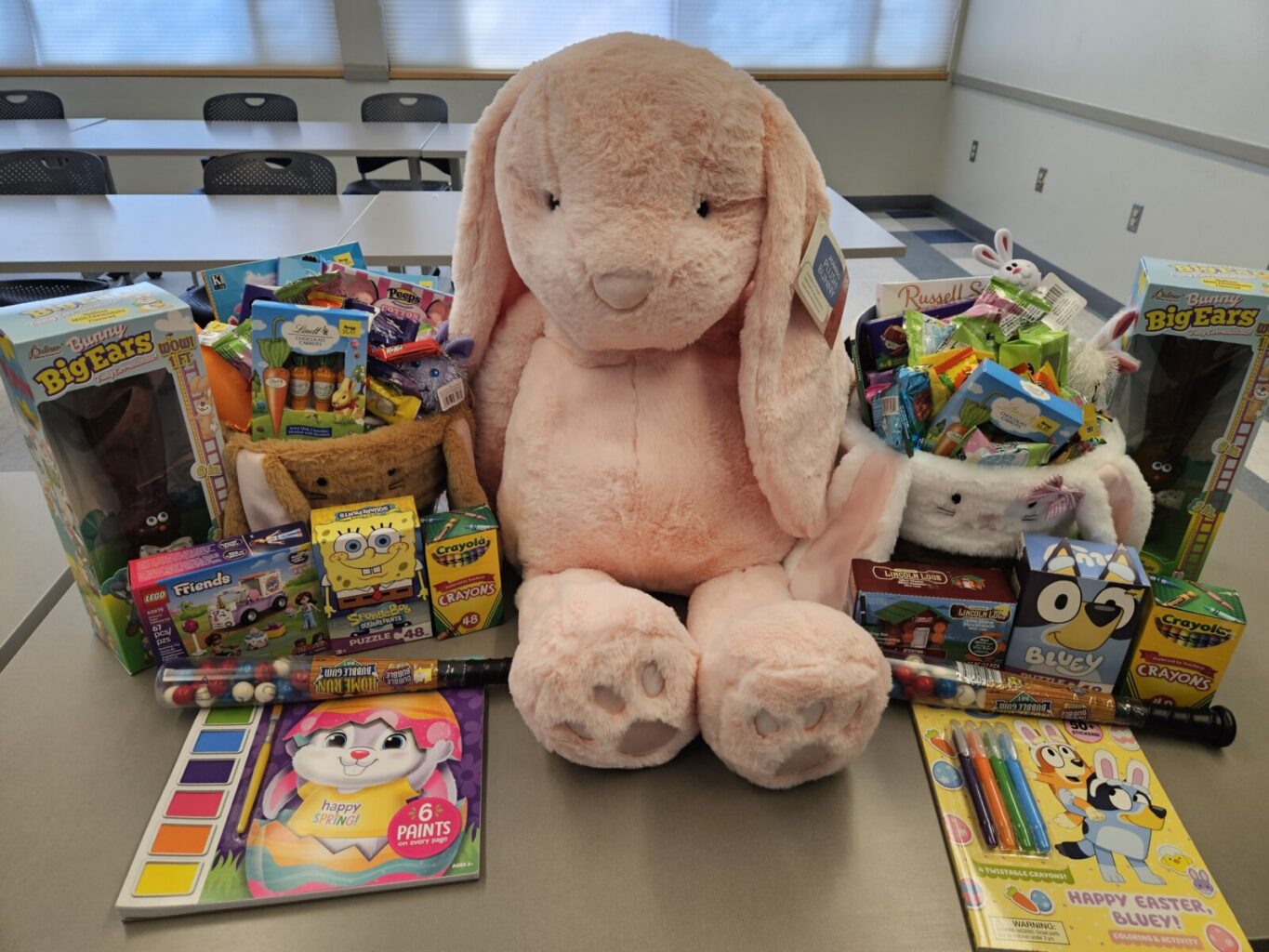 A large stuffed rabbit with two baskets of toys, candies, and activities for children. 