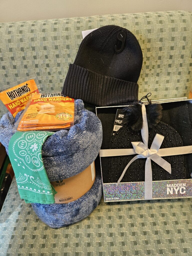 Picture of basket items such as a plush throw, a beanie, and hand warmers.