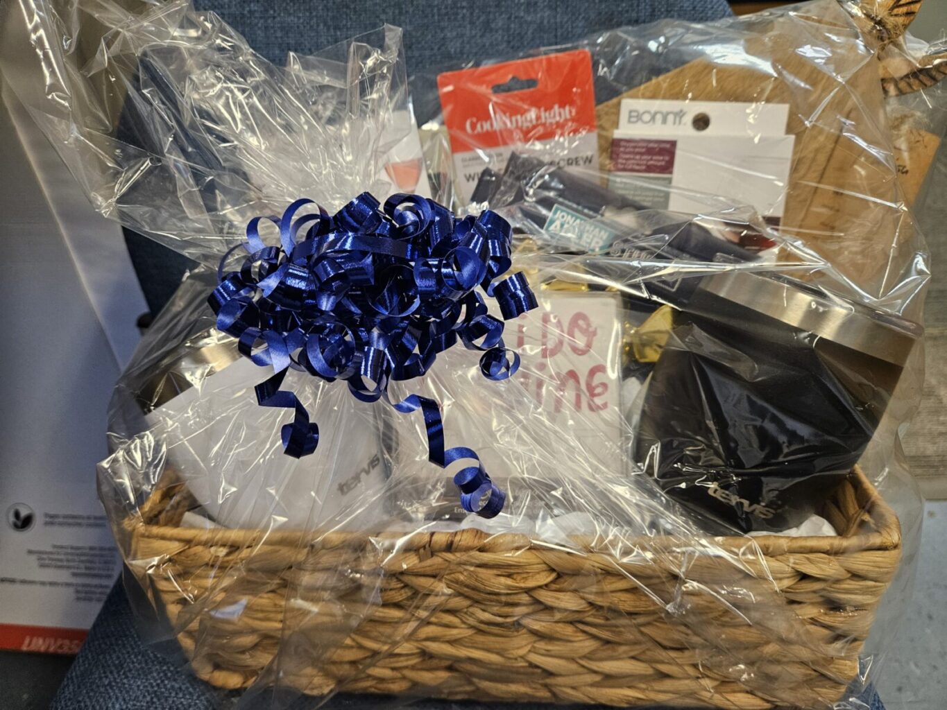 A gift basket featuring elements of a party plate, such as a serving board, corkscrew, and serving utensils.